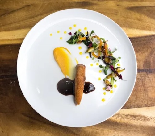 Amuse-bouche dressé : quenelle de purée orange, croustillant, sauce brune et pousses fraîches sur assiette blanche