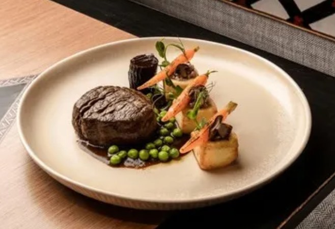 Filet de bœuf grillé, petits pois, jeunes carottes et pommes fondantes sur assiette crème