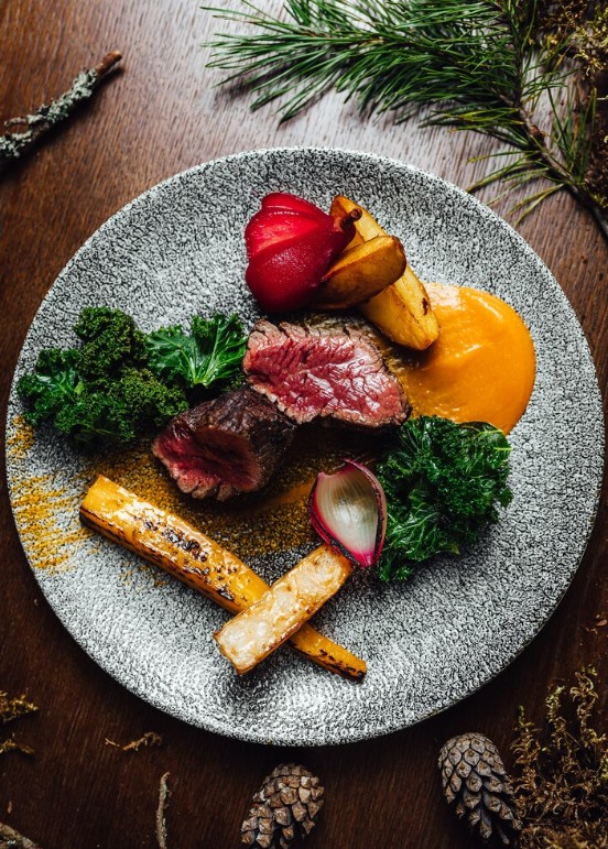Pièce de chevreuil rosée tranchée, poire pochée au vin rouge, panais rôti, chou kale et purée de courge sur assiette de grès