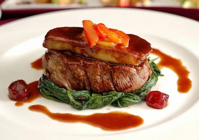Tournedos Rossini : pavé de bœuf surmonté de foie gras poêlé, sur un lit d'épinards, jus brillant et griottes